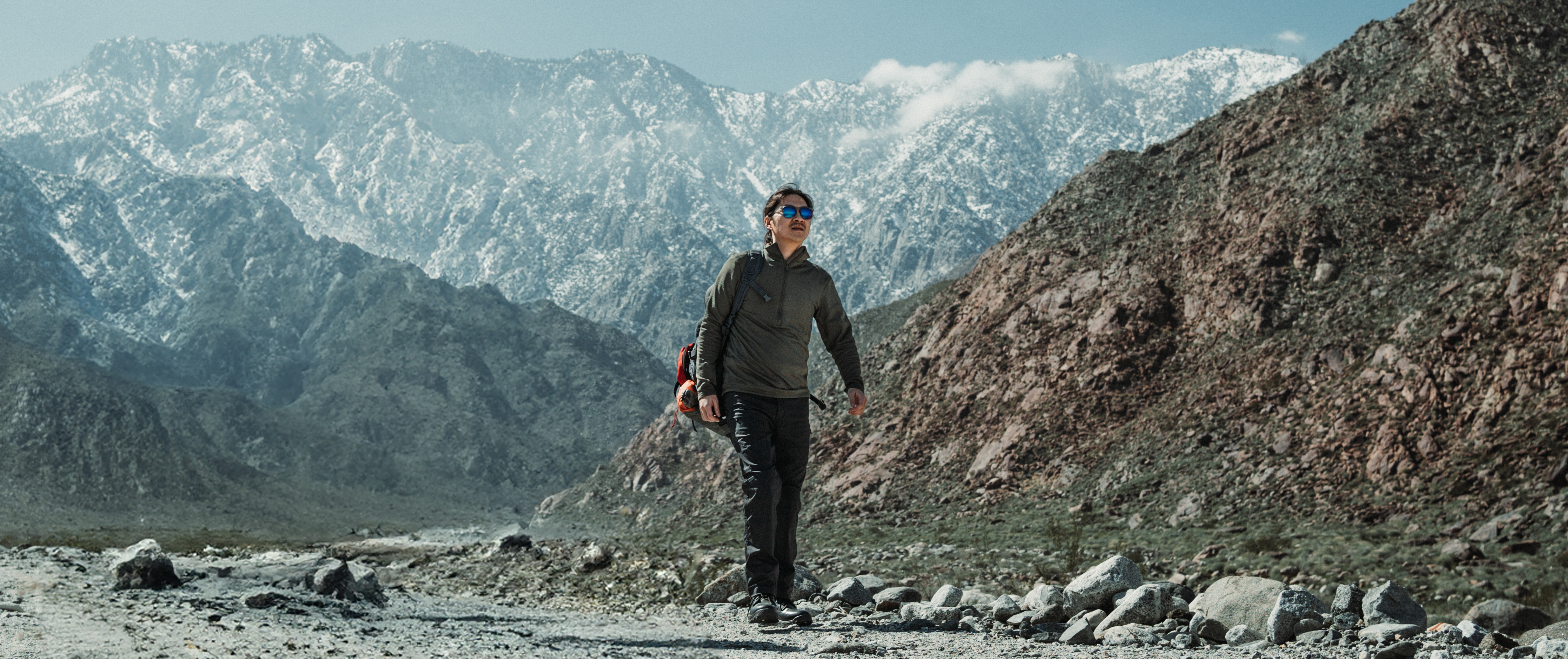 Image of a person walking with a large snowy mountain behind him while wearing a base II zip pullover