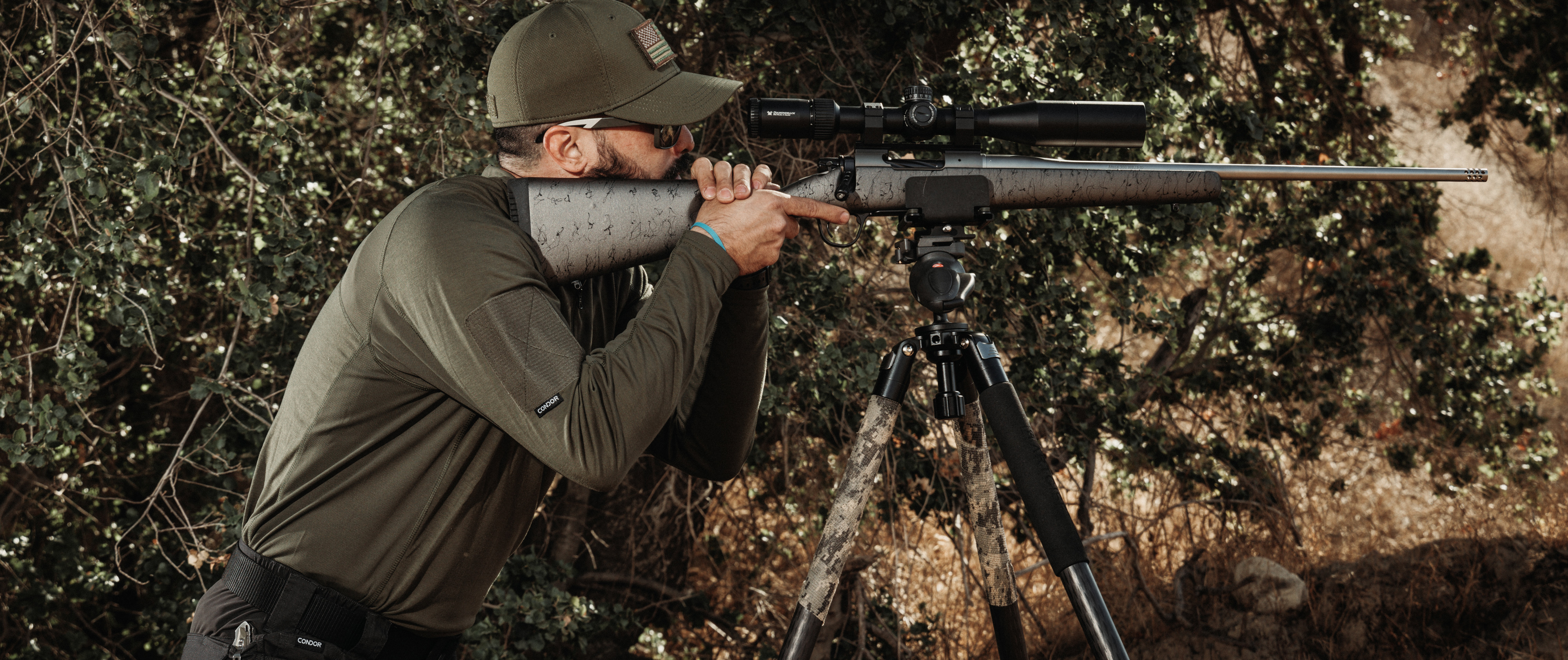 man about to shoot a long range rifle while earing a trident battle top